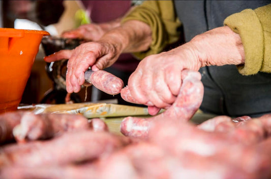 Artisan charcutier embossant à la main un saucisson artisanal dans un boyau naturel - Ôsaucissons